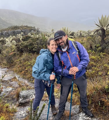 A smiling couple hiking with trekking poles on a foggy trail in the paramo mountains.