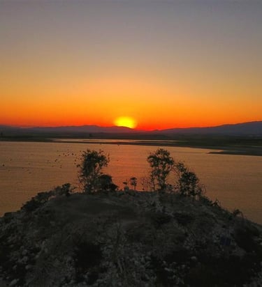 Golden sunset over a calm lake with a rocky island and silhouettes of trees against an orange sky.