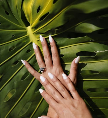 Manucure élégante en forme d'amande blanche sur une main ornée d'une bague rose argentée sur fond de