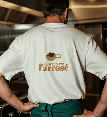 Un chef cuisinier portant un t-shirt blanc avec le logo du Coffee Shop l’Arrosé dans une cuisine pro