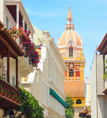 Historic street in Cartagena with colorful colonial architecture and the Santa Catalina Cathedral dome.