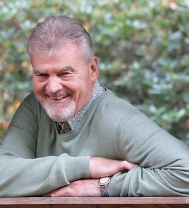 Willem lacht open en vriendelijk terwijl hij ontspannen leunt in een houten raamkozijn, omgeven door