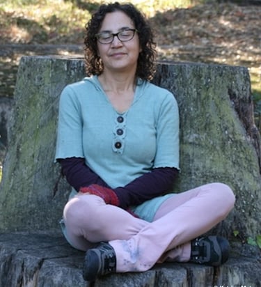 Katrina sitting on a tree stump with eyes closed smiling