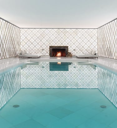 Luxury indoor pool area with white latticed walls and a marble fireplace.