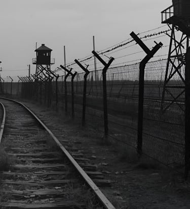 Black and white photo of a railway track running alongside a barbed wire fence and wooden watchtowers.