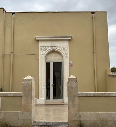 Minimalist beige building facade with an ornate white stone arched doorway and glass entry door.