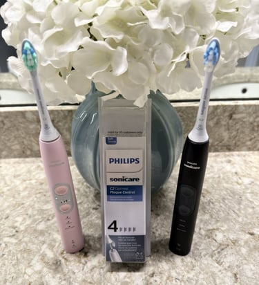 Two electric toothbrushes and open replacement head box on a clean bathroom counter with flowers