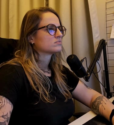 A woman with glasses and tattoos recording a podcast using a professional studio microphone.