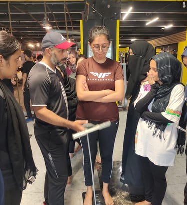 A gym trainer assists a young woman checking her on a BIA scale during a fitness assessment.
