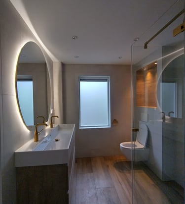 Moderne badkamer met een dubbele wastafel, daarboven een grote spiegel. Gouden kranen. Nis met verli