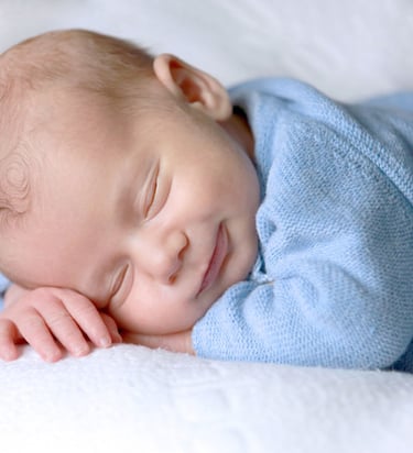 a happy baby sleeps on a blanket in a bed