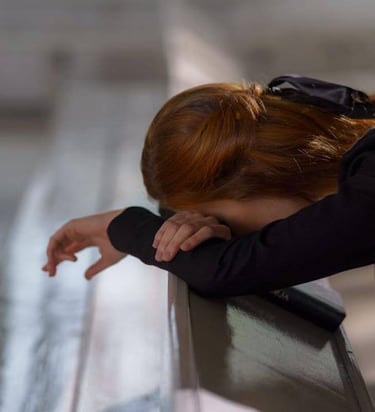 Individual resting head on crossed arms in a church pew, beside a book, in quiet reflection.