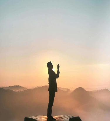 Person silhouetted against sunrise on a flower-shaped platform above misty hills.