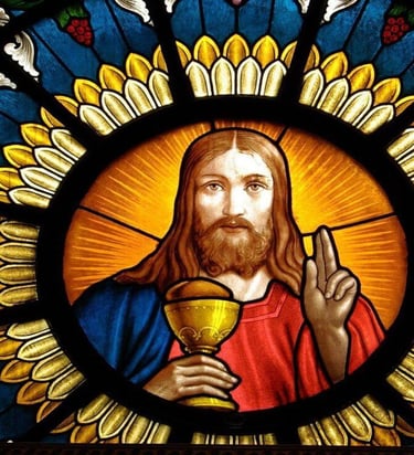 Stained glass window showing Jesus with a chalice and blessing gesture, surrounded by vibrant symbol