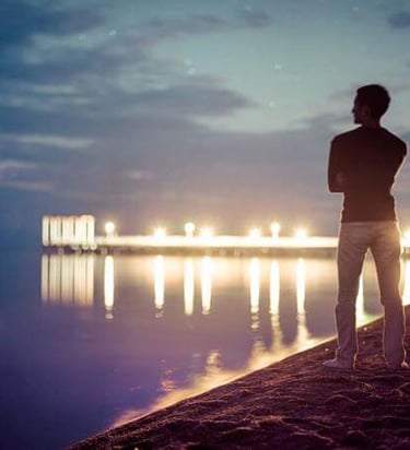 Person standing by water at night, reflecting quietly, symbolizing searching or contemplation.