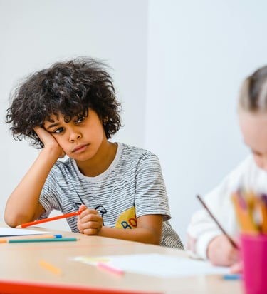 Criança com expressão de desatenção e cansaço em sala de aula, ilustrando dificuldades escolares e sintomas de TDAH.