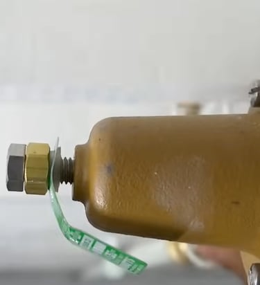 Close-up of a yellow water pressure reducing valve with brass adjustment bolt and safety seal.