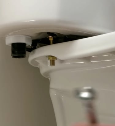 A close-up of a person installing a toilet tank to the bowl with brass bolts for repair.