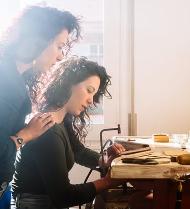 Instructora guiando a una participante durante un taller artesanal en mesa de trabajo.
