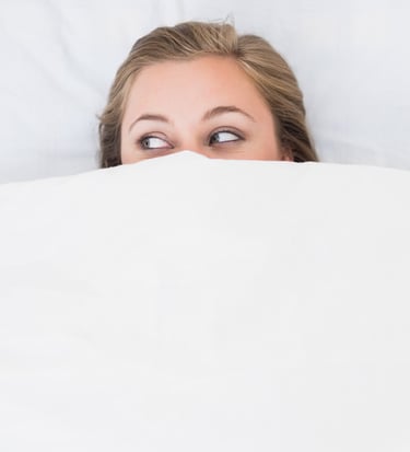 a woman is peeking behind a blanket in a bed