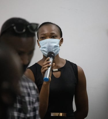 a woman in a black dress and face mask speaking into a microphone