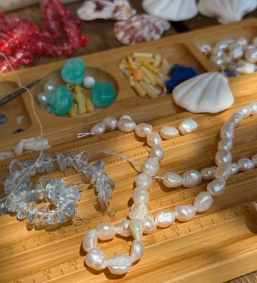 Handmade jewelry making process with freshwater pearls and sea glass on a wooden bead board.