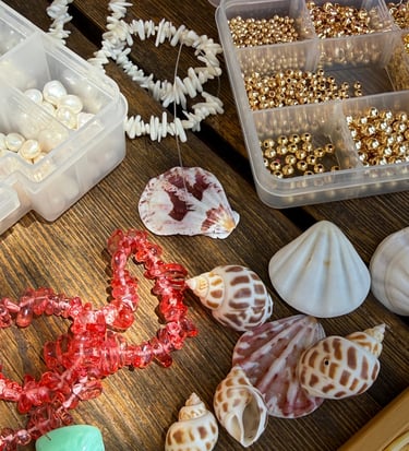 Jewelry making supplies with sea shells, gold beads, and white pearls for DIY shell necklaces.