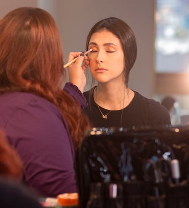 Maquilladora profesional que aplica sombra de ojos dorada a una modelo usando un pincel difuminador.