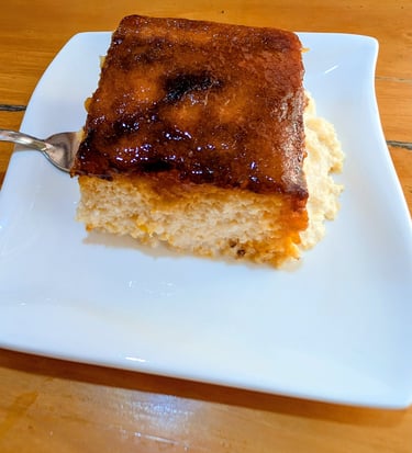 A slice of moist tres leches cake with a caramelized sugar topping served on a white square plate.