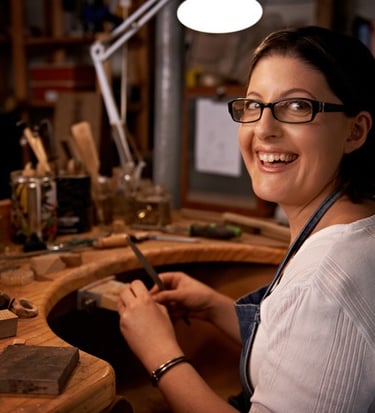 Una joyera artesana sonriente trabajando en un banco de trabajo de madera con herramientas
