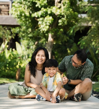 Parents sitting with their child on a garden pathway during a family photography session at The Meru Sanur Bali