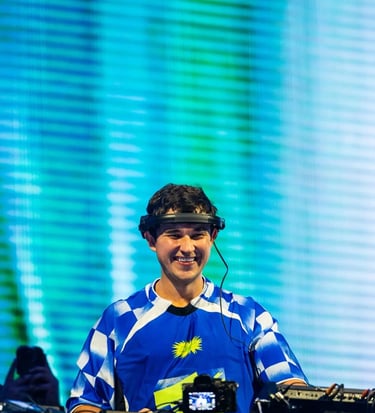 john summit in a blue shirt and headphones on a dj booth