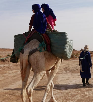 Two people atop a camel laden with baggage in the Moroccan Sahara desert