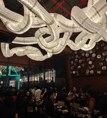 Crowded modern restaurant interior featuring a large wavy paper lantern light fixture and decorative plate wall art.
