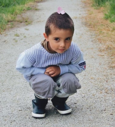 a young boy is sitting on a gravel road