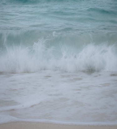 Slow shutter image of waves crashing on beach, pastel blues.