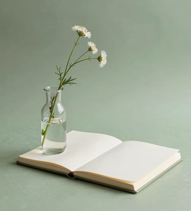 A minimalist still-life photograph featuring a delicate glass vase with a single wildflower branch, set beside a handmade sketchbook. The colors are soft moss green and creamy off-white, with clean lines and soft natural lighting.