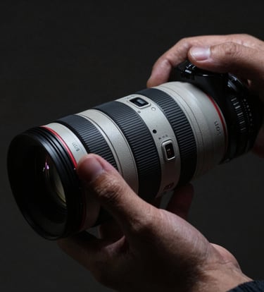 Close-up of a photographer's hand adjusting a high-end lens in a dimly lit North American studio. The lighting is dramatic and moody, with deep shadows and soft highlights of light gray on metallic surfaces.