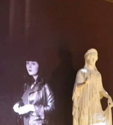 Projection of Tina Bikic beside a classical statue in a museum installation.