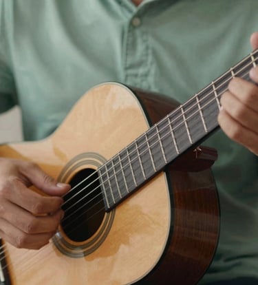 A close-up shot of Lyan Galindo's hands gracefully playing a classical guitar. The lighting is intimate and warm, emphasizing the texture of the strings and the motion. Incorporates #91AA9D sage tones in the background fabric for a sophisticated, calming feel.