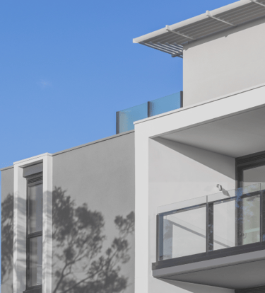 Modern apartment building with white and grey facade and glass balcony against a clear blue sky.