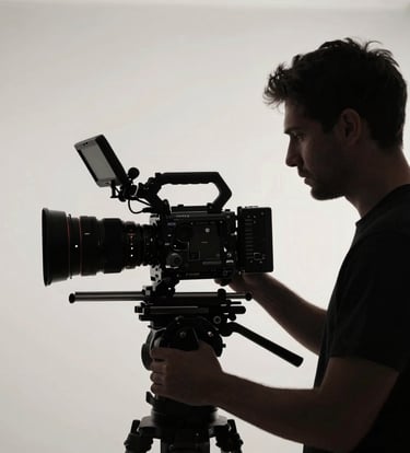 A professional cinematographer in a North American / US studio setting, silhouetted against a soft off-white light source while operating a premium camera rig. Deep black and charcoal grey tones dominate the sleek composition.