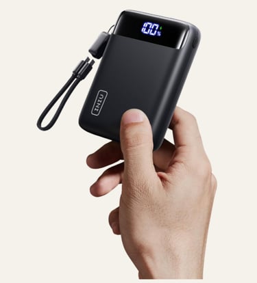 Hand holding a compact black INIU portable charger with a digital LED display showing 100 percent battery life.