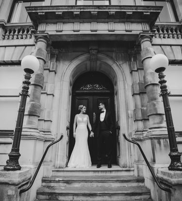 Black and white photo of bride & groom standing at a grand building entrance,captured by Fred Studio