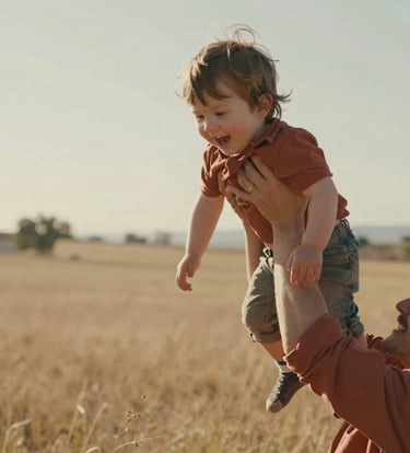A candid, cinematic close-up of a young child being lifted into the air by a parent in a sun-drenched North American / US meadow. The lighting is warm and hazy, with terracotta and soft sand tones in the clothing and surroundings, highlighting an authentic moment of joy.