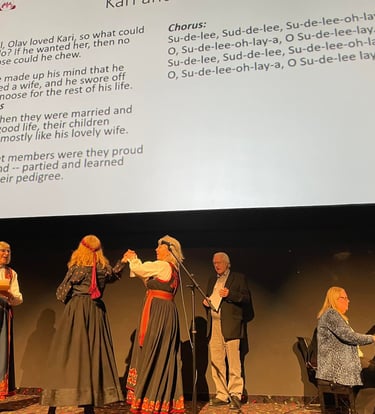 a woman in bunad singing, a man singing and two women in bunad dancing