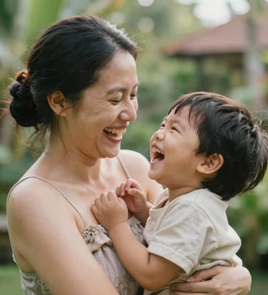 An intimate, close-up shot of a mother and child laughing in a Bali garden. Soft, natural morning light, warm skin tones, and subtle hints of #F8F5EF in the clothing. Elegant and authentic composition.