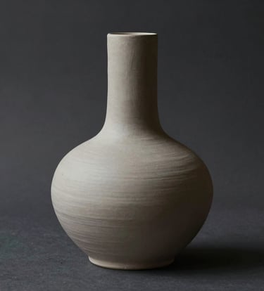 A minimalist ceramic sculpture with organic, fluid lines. The piece is a soft #C8C0B2 color, set against a deep #1A1A1A shadow. The lighting is focused and contemplative, highlighting the physical texture of the clay.
