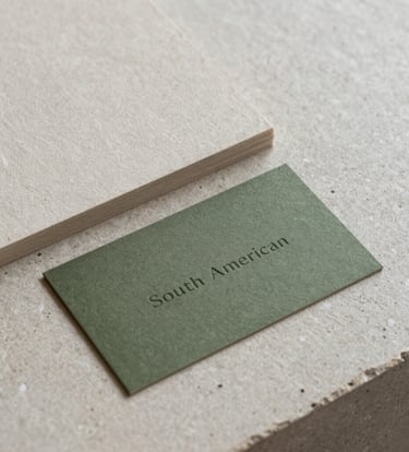 Close-up photography of high-quality tactile paper samples and a minimalist olive green business card on a light gray stone surface, soft natural lighting, South American design studio setting.