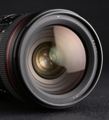 A close-up photograph of a professional camera lens reflecting a soft, warm cream glow, set against a deep charcoal black background. The style is sharp, clean, and luxurious, representative of a North American / European professional studio.